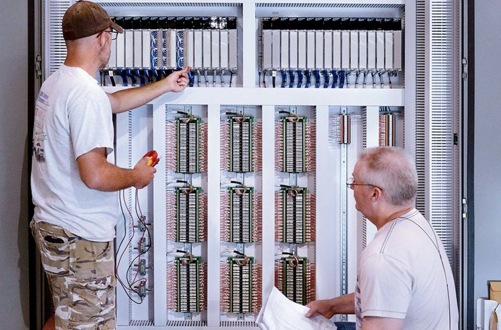 Two men working on the wiring of a panel